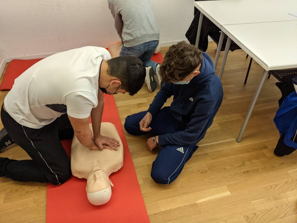 Two students practicing CPR chest compressions on a mannequin