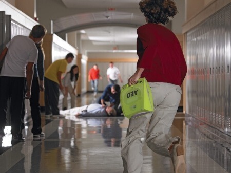 Teacher running down hallway with AED toward a man on the floor